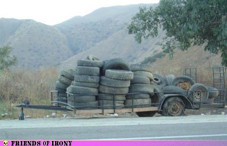 Trailer loaded with used tires sitting on the side of the road with a flat tire